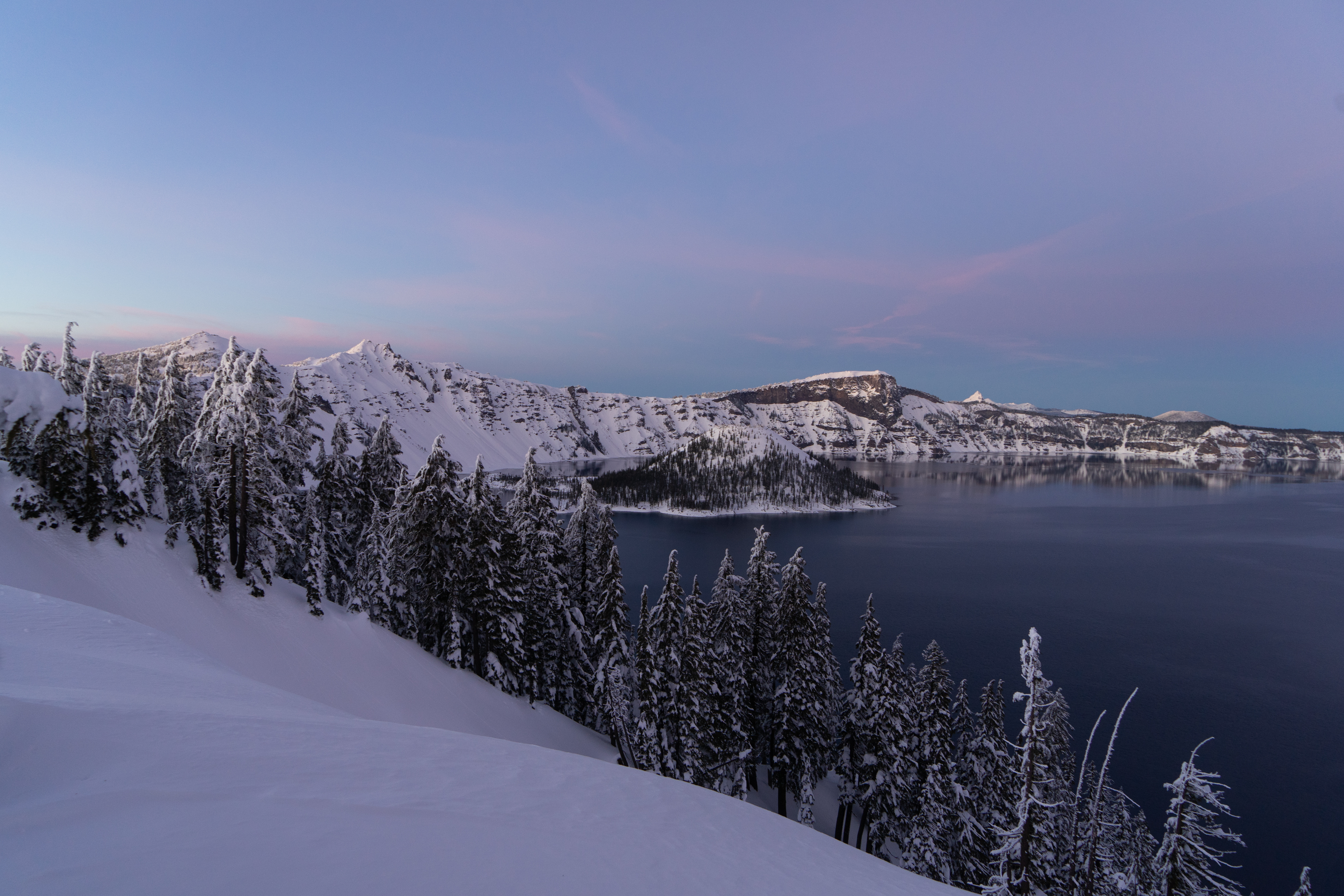 Snow-covered cliffs surrounding the blue water of Crater Lake